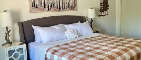 Een slaapkamer met een bed, twee nachtkastjes, een plafondventilator en een kunstwerk aan de muur.