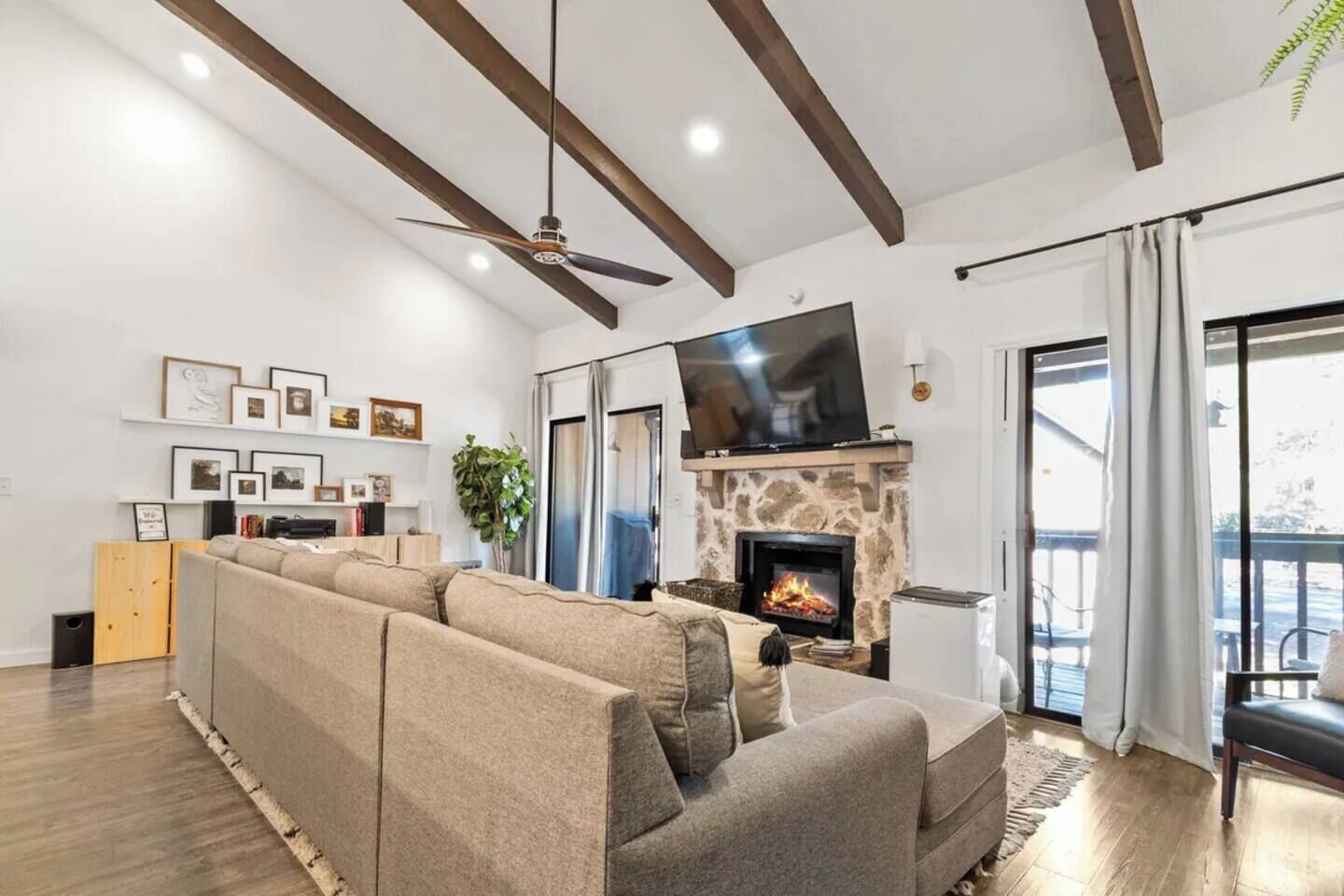 A living room with a sofa, fireplace, TV, and a balcony with curtains.
