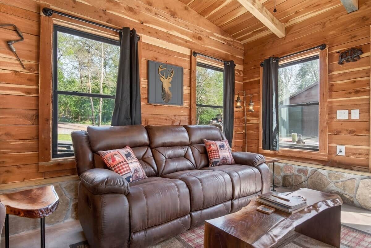 A wooden cabin interior with a leather sofa, stone accents, and large windows.