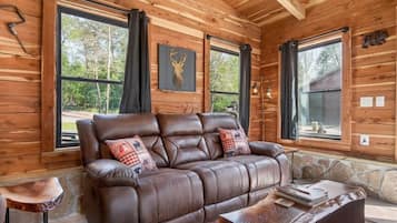 A wooden cabin interior with a leather sofa, stone accents, and large windows.