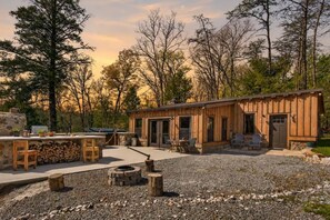 A rustic cabin with a stone fireplace, outdoor seating, and a gravel patio. - Stagecoach Saloon Riverside cabin with stone pizza oven (Cumberland County)
