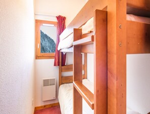 Ein Schlafraum mit Etagenbetten, einem Fenster, einer Heizung und Blick auf einen Wald.