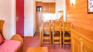 A compact room with a bed, a dining table with chairs, wooden cabinets, and a red door. - Family Apartment 60 m From Ski-slope (Modane)