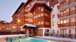 A hotel with a swimming pool surrounded by snow, wooden balconies, and a ski slope in the background. - Family Apartment 60 m From Ski-slope (Modane)