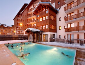 Ein Hotel mit Schwimmbad, umgeben von Schnee, hölzernen Balkonen und einer Skipiste im Hintergrund.