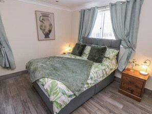 Een slaapkamer met een bed, nachtkastje, lamp en een raam met gordijnen.