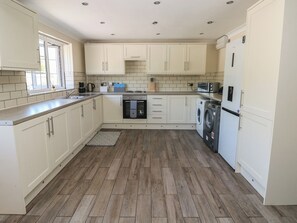 A kitchen with white cabinets, a dishwasher, a washing machine, a microwave, and a window. - Annexe @ Meadows Farm (Swansea)