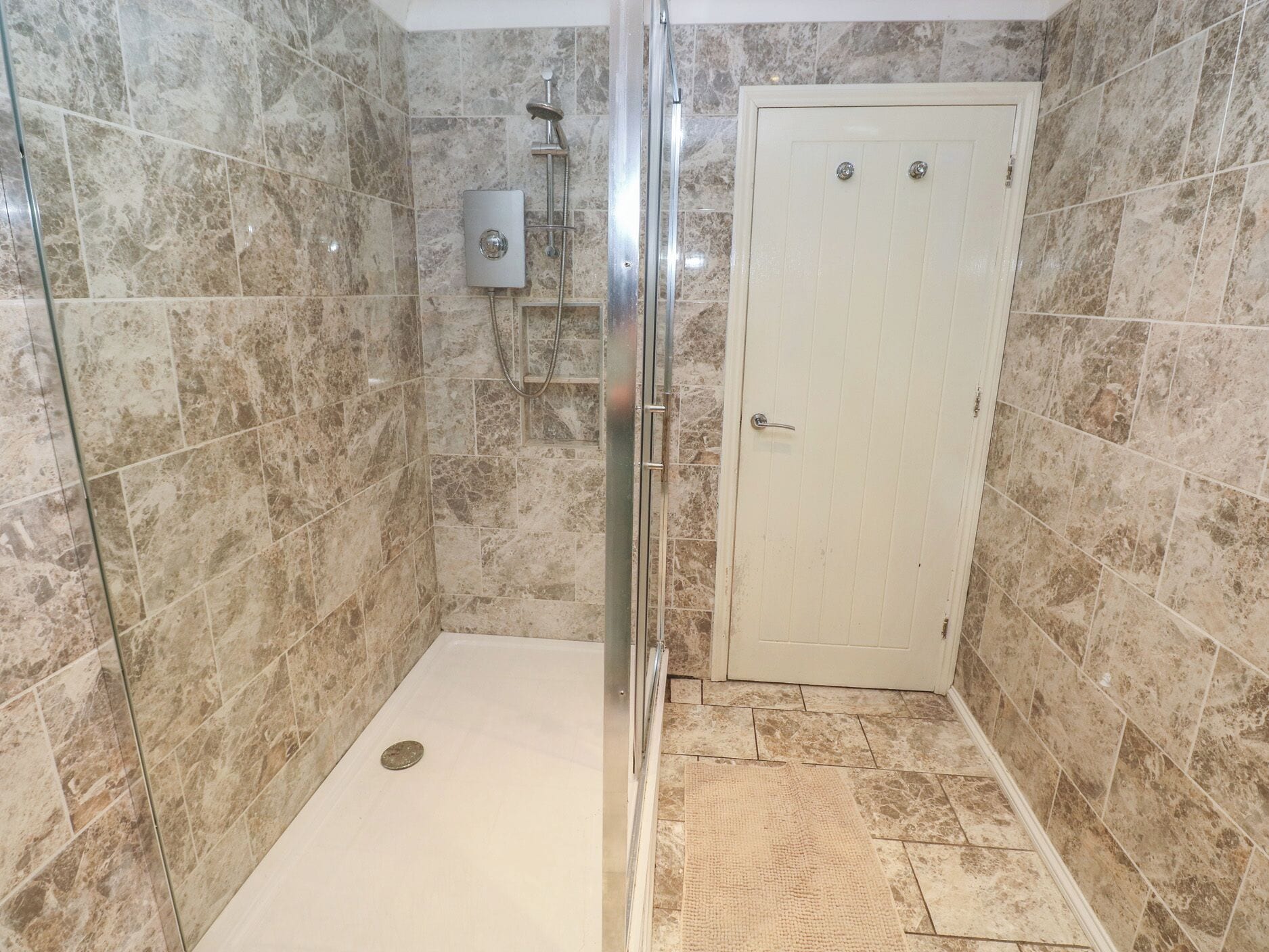 Une salle de bain avec une douche, des murs carrelés, une porte et un tapis de sol.
