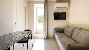 Ein kompakter Wohnbereich mit einer Couch, einem an der Wand befestigten Fernseher und einer Essecke mit Tisch und Stühlen.