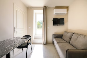 A compact living space with a sofa, a television mounted on the wall, and a dining area with a table and chairs. - Diamond 14 Apartment (Cannes)