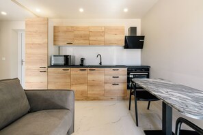 A modern kitchen with wooden cabinets, a built-in microwave, and a dining area with a marble table. - Diamond 14 Apartment (Cannes)
