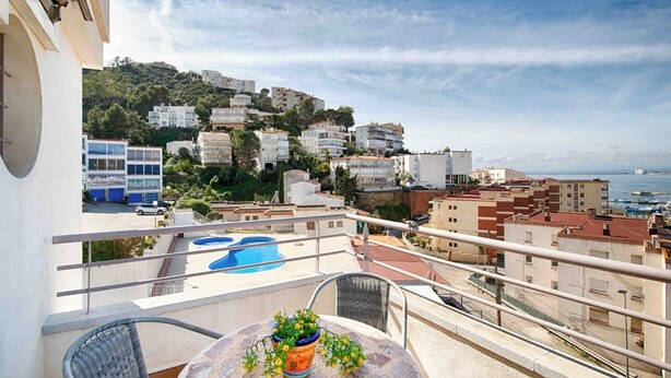 A balcony with a pool, a table with a potted plant, and a view of buildings and the sea. - Apartment with ocean views, a 10-minute walk from the waterfront (Roses)