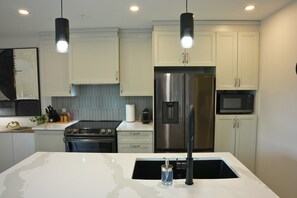 A modern kitchen with stainless steel appliances, white cabinetry, and pendant lighting. - Le 102 Condo moderne au cœur de Magog (Magog)