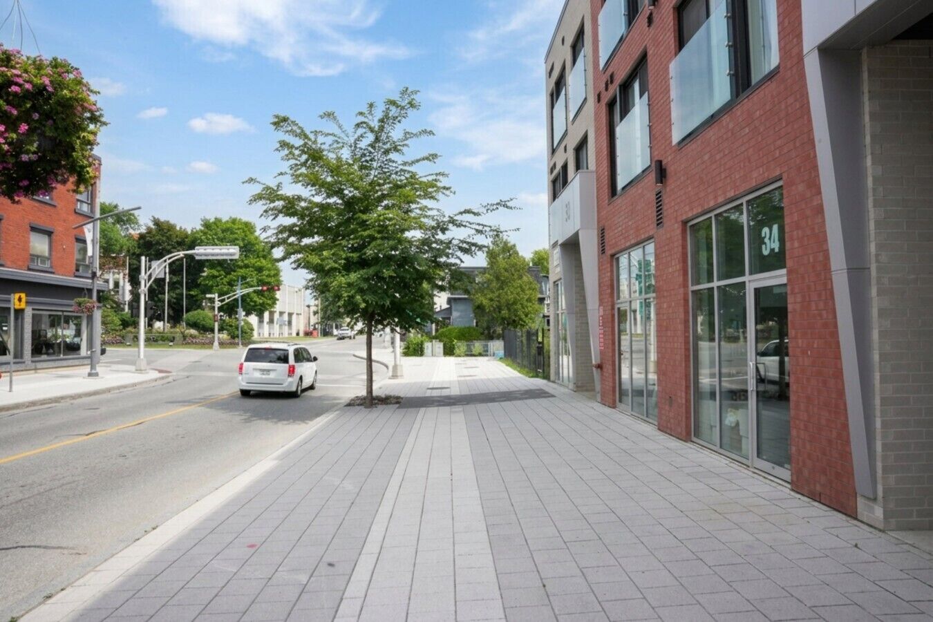 Un edificio moderno con amplios ventanales, aceras pavimentadas y un árbol en primer plano.