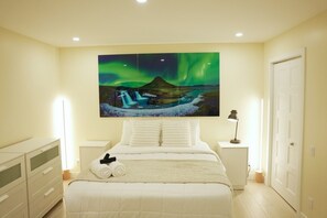 A bedroom with a bed, a nightstand, a lamp, a dresser, and a painting of the Northern Lights. - Le 102 Condo moderne au cœur de Magog (Magog)