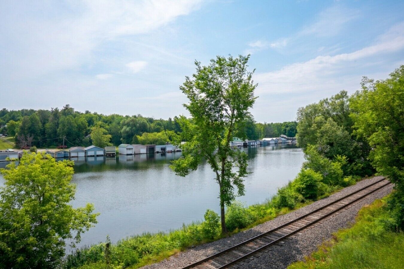 Une vue sur un lac, avec une voie ferrée, des bateaux et une zone boisée.