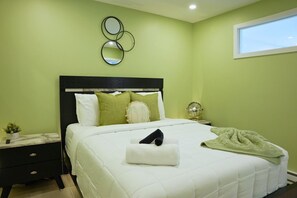 A neatly made bed with pillows, a bedside table with a lamp, and a window with a view. - Le 102 Condo moderne au cœur de Magog (Magog)