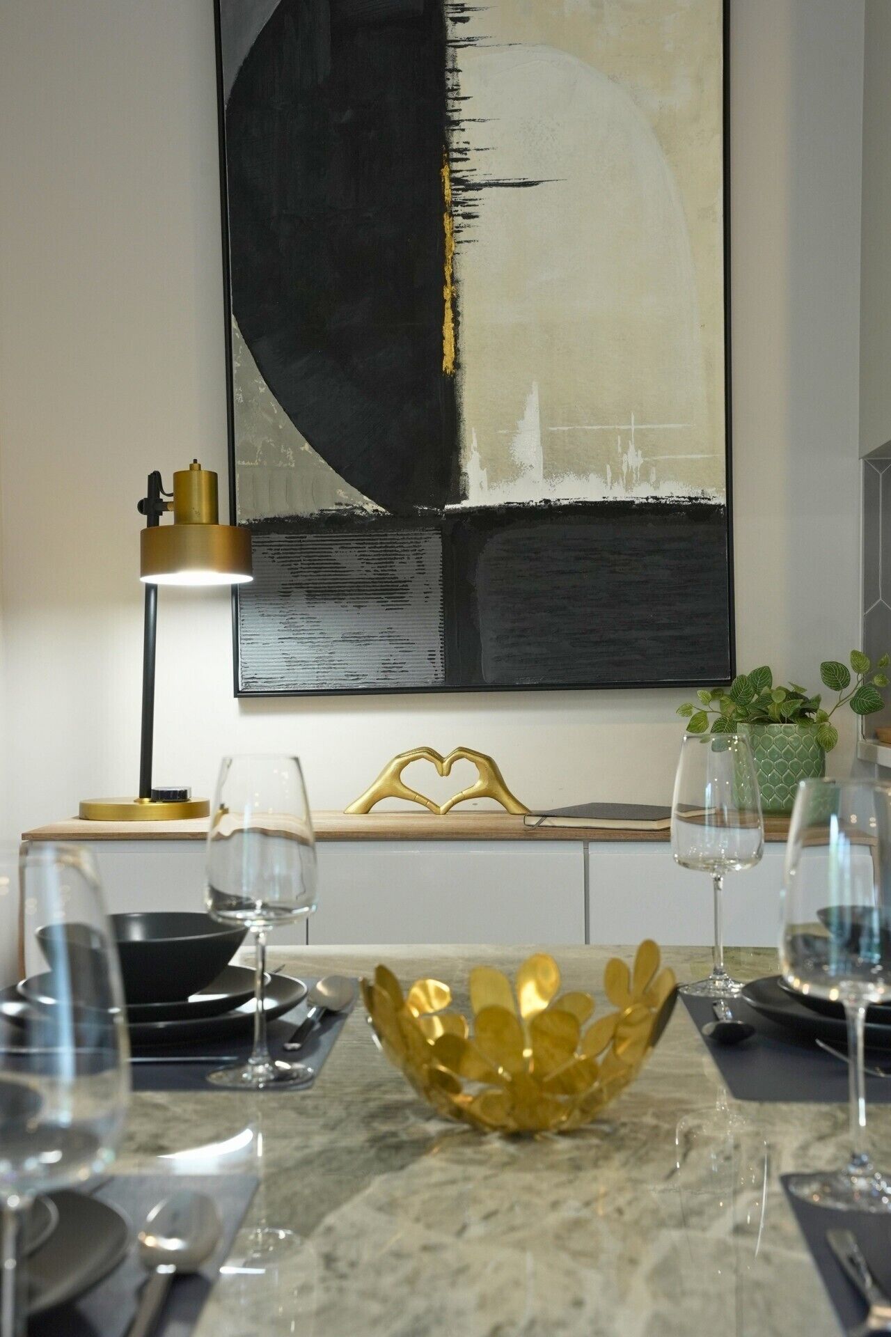 Un espace de salle à manger moderne avec une table en marbre, un centre de table en forme de bol doré et un grand tableau abstrait accroché au mur.