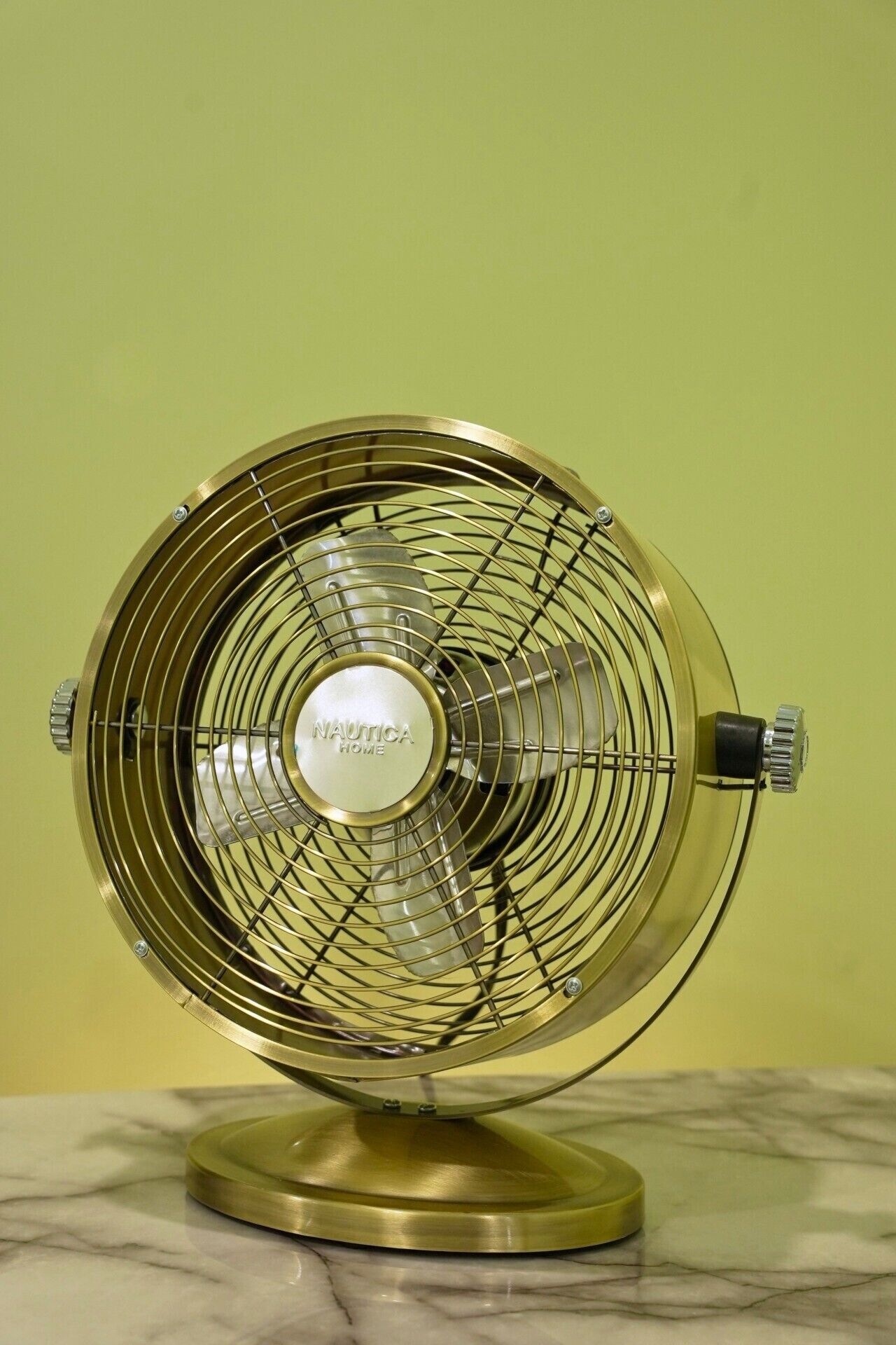 A vintage Nautica Home fan with a metallic finish, placed on a marble surface against a plain background.