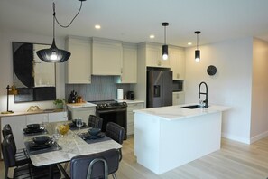 A modern kitchen with a central island, white cabinetry, and pendant lighting. - Le 102 Condo moderne au cœur de Magog (Magog)
