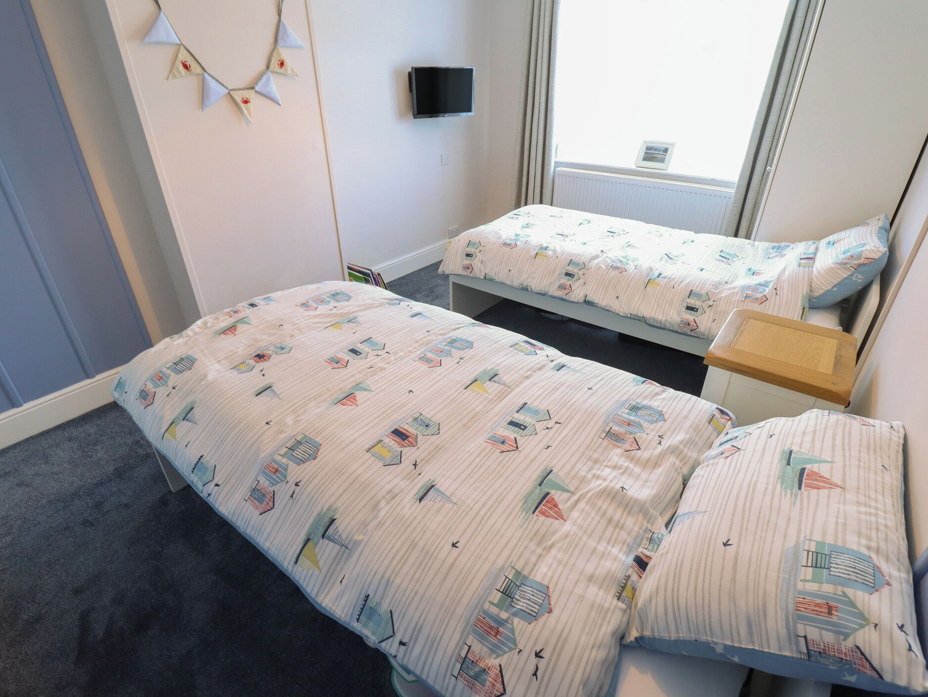 Ein Zimmer mit zwei Betten, einem Fernseher an der Wand und einem Fenster mit Vorhängen.