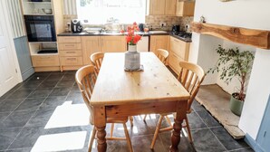 Una cocina con armarios de madera, una mesa de comedor con sillas, un jarrón con flores y una planta en maceta.