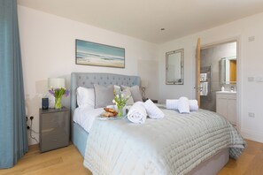 A neatly arranged bedroom with a bed, bedside tables, a mirror, and a view of the bathroom. - 2 Remera (St Ives)