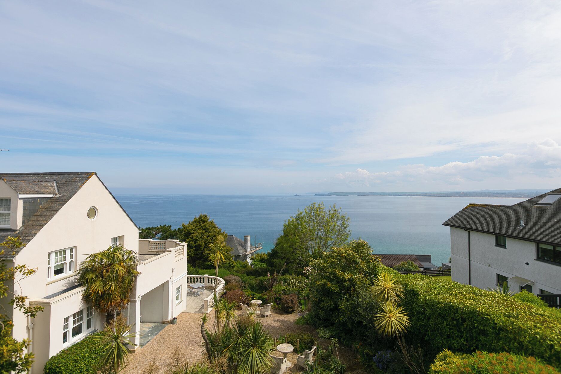 A coastal residential area with houses, a patio with chairs, and a view of the sea.