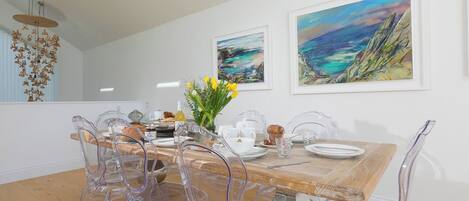 A dining area with a wooden table, clear chairs, and artwork on the walls.