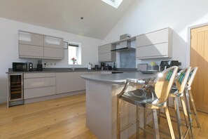 A modern kitchen with a central island, bar stools, and a skylight. - 2 Remera (St Ives)