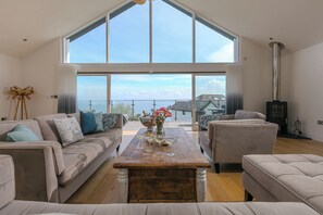 A spacious living room with a high ceiling, large windows, a fireplace, and a view of the sea. - 2 Remera (St Ives)