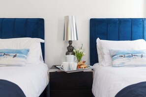 A hotel room with two beds, a nightstand with a lamp, a tray with breakfast items, and a vase with flowers. - 2 Remera (St Ives)
