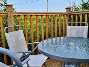 A wooden deck with a round glass table and two white mesh chairs.