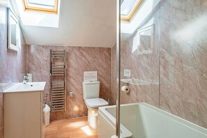 A modern bathroom with a marble wall, a glass shower enclosure, a toilet, and a sink.