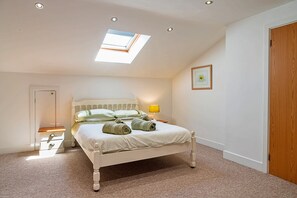 A bedroom with a skylight, a bed with towels, a bedside table with a lamp, and a door.