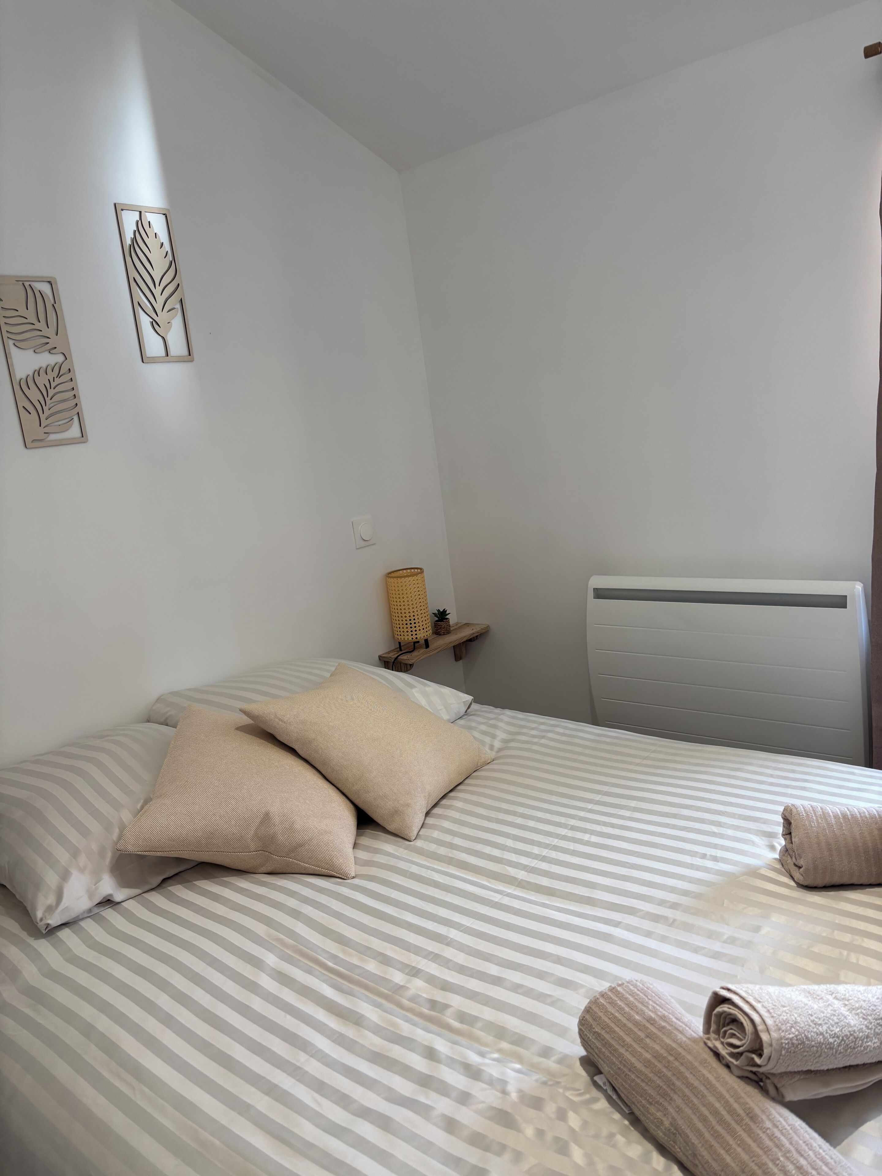 En pænt redt seng med stribet sengetøj, et lille natbord med en lampe, og et billede på væggen.
