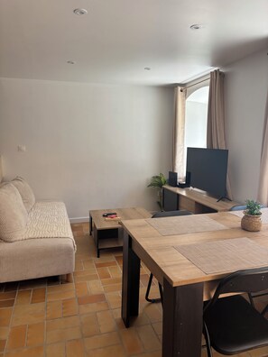 Ein modernes Wohnzimmer mit einer Couch, einem Holzesstisch, einem Fernseher und einer Zimmerpflanze.