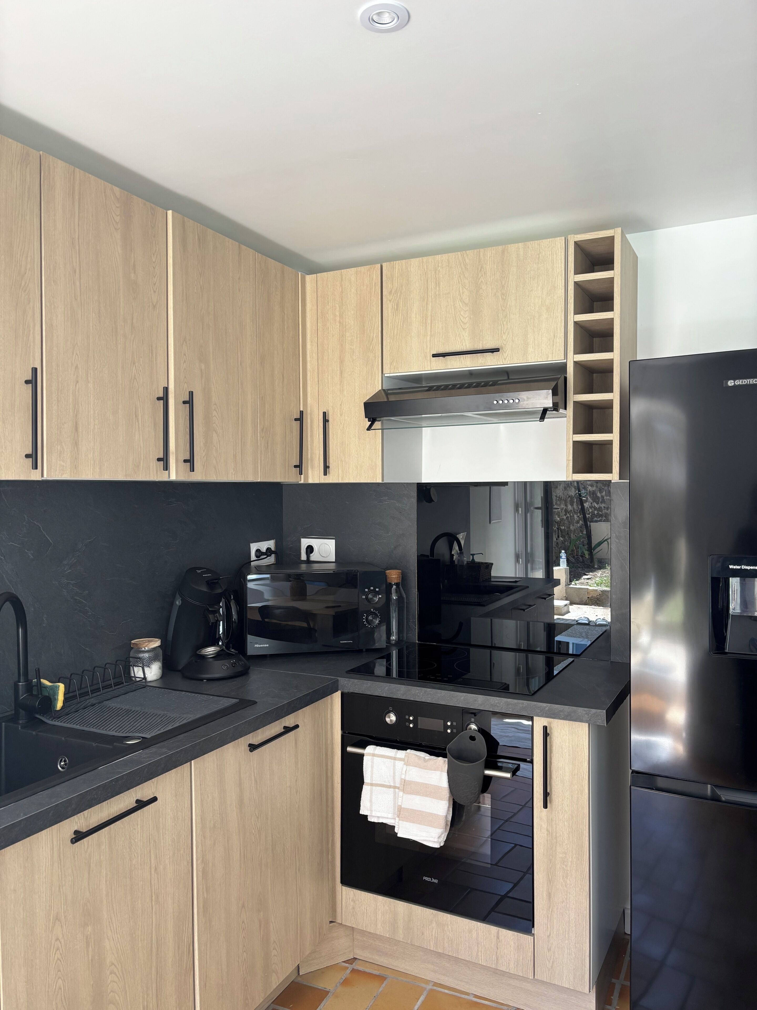 A modern kitchen with wooden cabinets, a built-in oven, a coffee machine, and a water dispenser.
