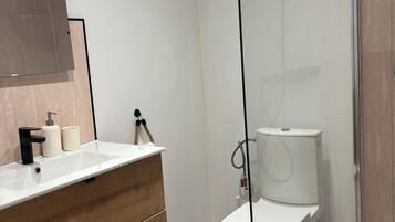 Une salle de bain moderne avec un meuble-lavabo blanc, une cabine de douche en verre et des toilettes.