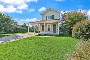 A two-story house with a covered porch, a well-maintained lawn, and a clear sky. - Pecan Pointe Cottage - Pet Friendly (Brunswick)
