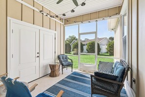 A covered porch with a sliding glass door, wicker furniture, and a blue striped rug. - Pecan Pointe Cottage - Pet Friendly (Brunswick)