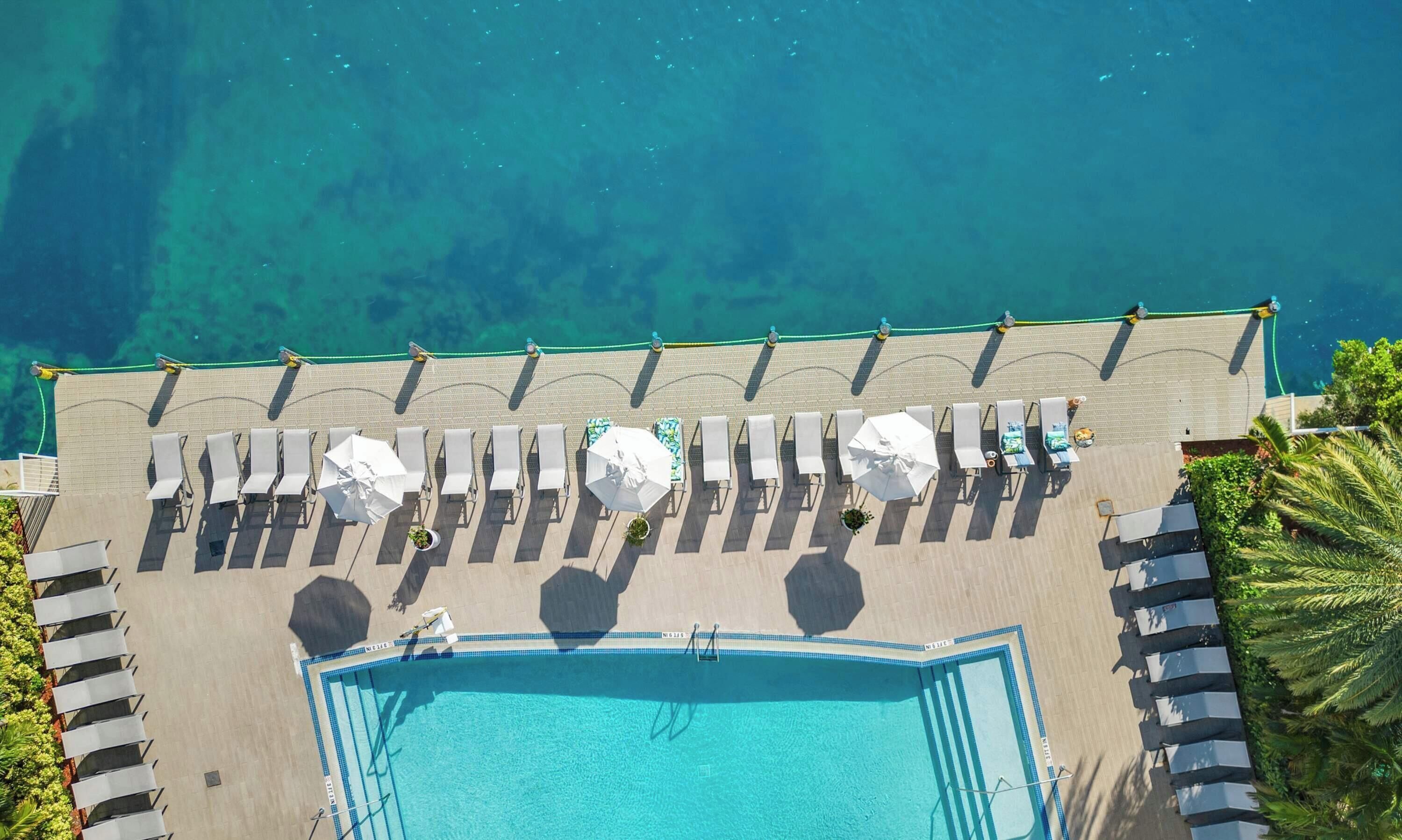 Ein Luftbild eines Resorts mit Schwimmbad, Liegestühlen und Strand.