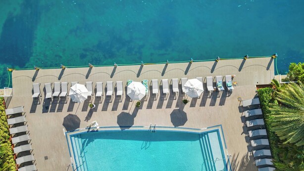Oversigtsbillede af et feriested med swimmingpool, liggestole og en strand.