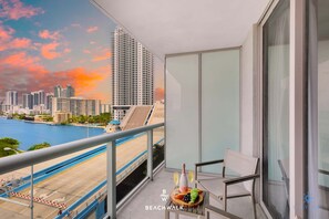 A balcony with a city view, a table with a bottle and glasses, and a fruit platter. - Sleek Studio with Intracoastal View & Pool (Hallandale Beach)