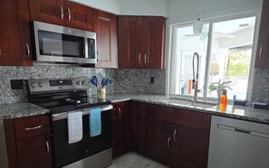 A kitchen with dark wooden cabinets, a stainless steel microwave, a stove, and a window with a view of the outdoors. - Charming 3-bedroom house with AC in terrific Sarasota (Sarasota)