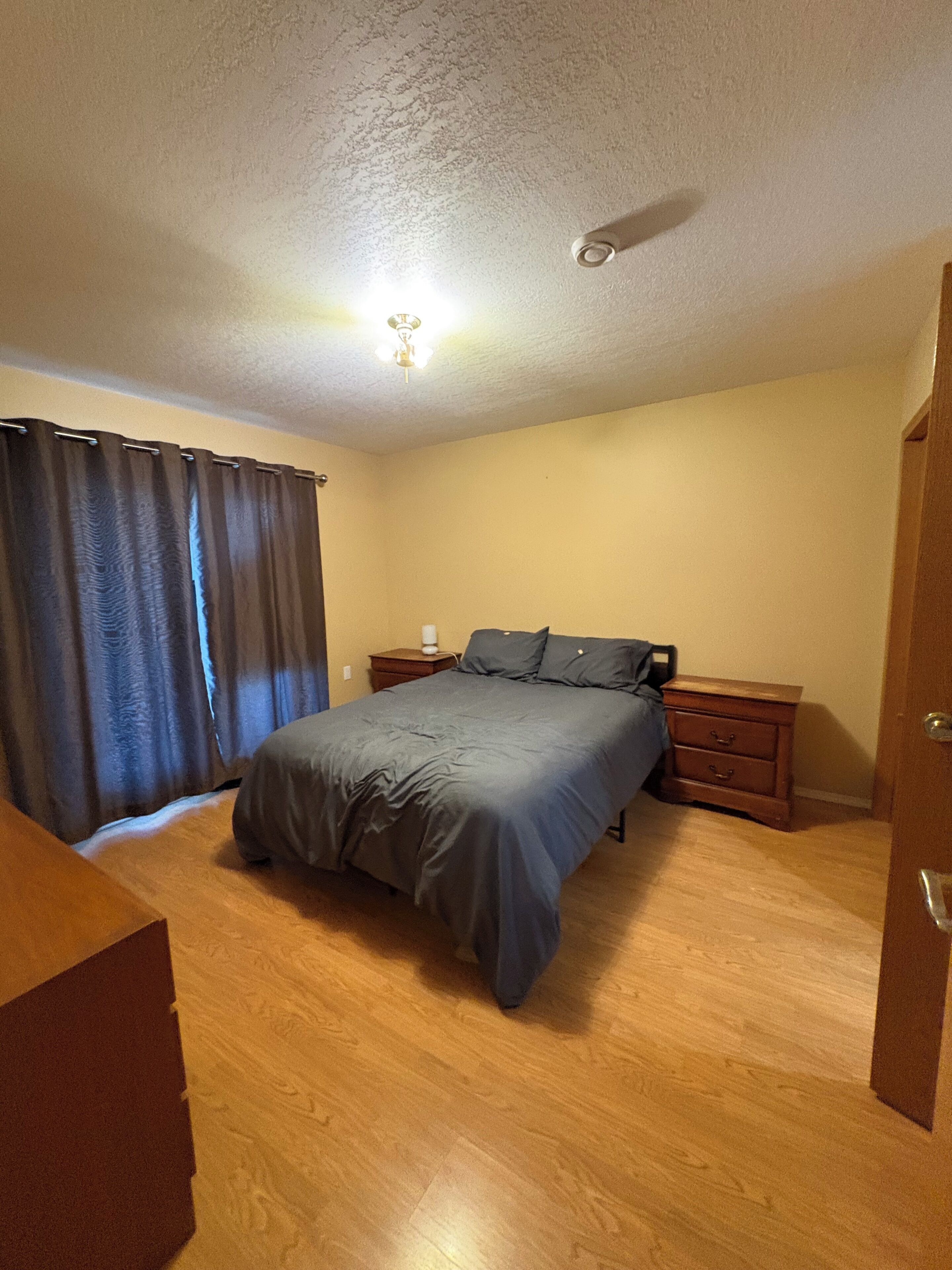 A bedroom with a bed, nightstands, a wooden dresser, and a ceiling fan.