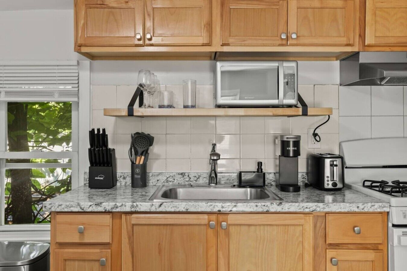 A kitchen with wooden cabinets, a stainless steel sink, a microwave, a toaster, and a coffee maker.
