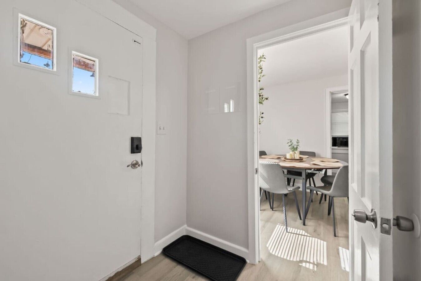 A hallway with a door leading to a dining area with a table and chairs.