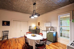 A dining area with a round table, chairs, a ceiling light fixture, and a kitchen adjacent to the dining area.