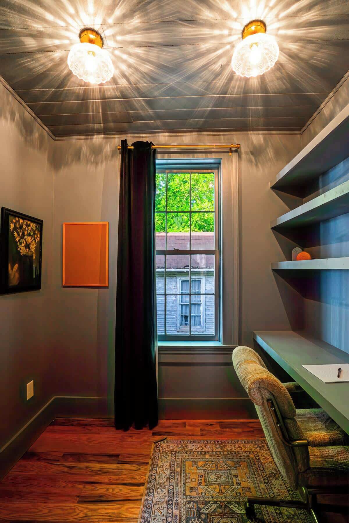 A room with a window, a chair, a rug, and a shelf.